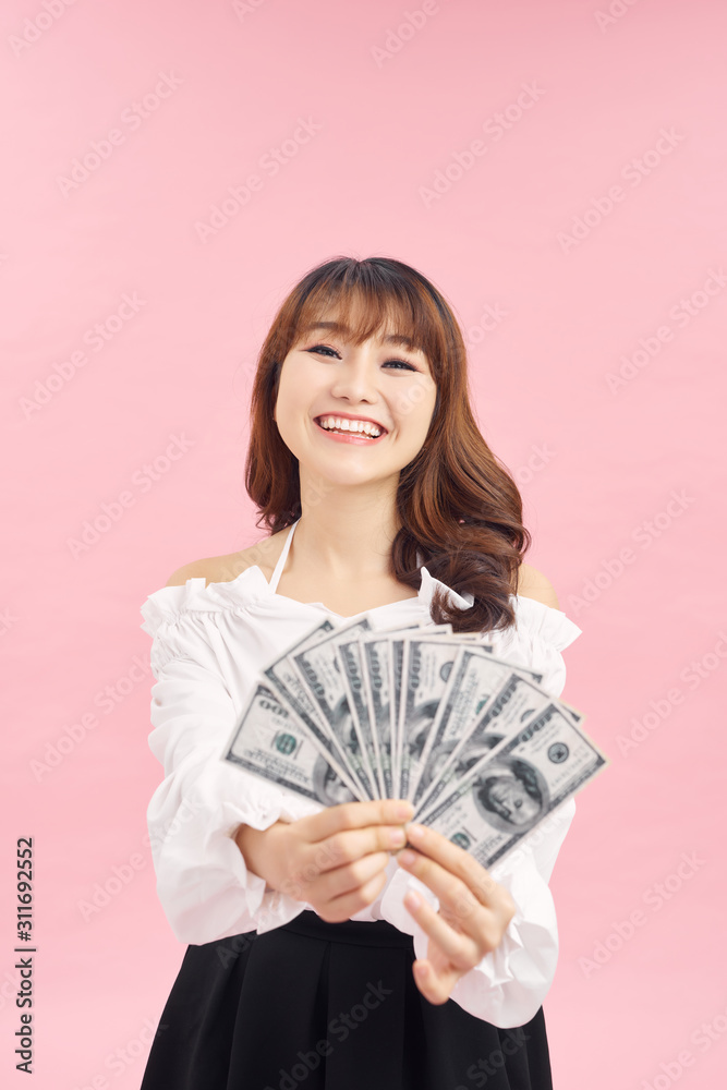 Image of delighted woman wearing basic clothes smiling and holding money cash isolated over pink background Image of delighted woman wearing basic clothes smiling and holding money cash isolated over pink background