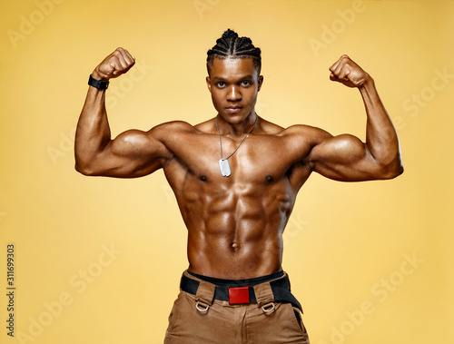 Athletic man posing. Photo of man with perfect physique on yellow background....