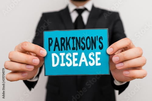 Writing note showing Parkinson S Is Disease. Business concept for nervous system disorder that affects movement Male human wear formal work suit with office look hold book