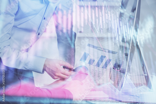 Double exposure of chart with businessman typing on computer in office on background. Concept of hard work.