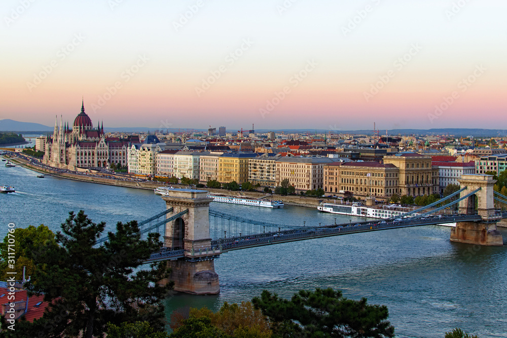 Fototapeta premium Aerial landscape view of Budapest. Picturesque view of Chain Bridge over Danube River and The Hungarian Parliament Building in the background. Scenic autumn sunset colors. Budapest, Hungary