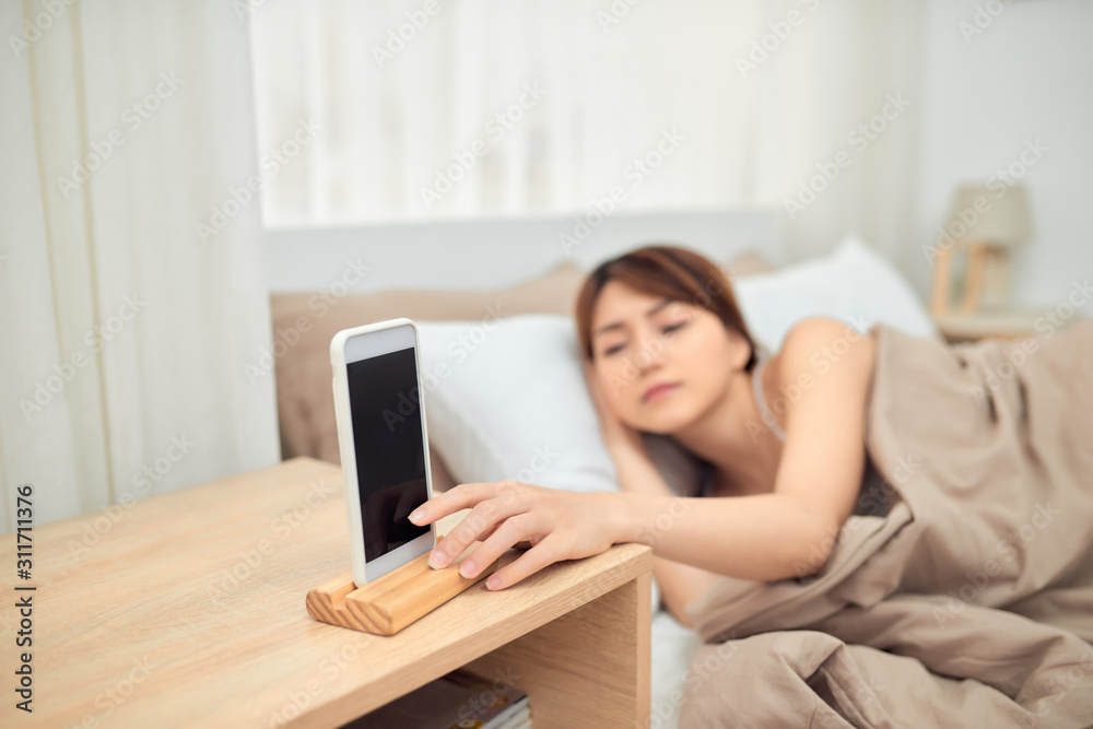 Annoying alarm. Woman lying in bed being woken by mobile phone, turning off noisy signal, closeup Annoying alarm. Woman lying in bed being woken by mobile phone, turning off noisy signal, closeup