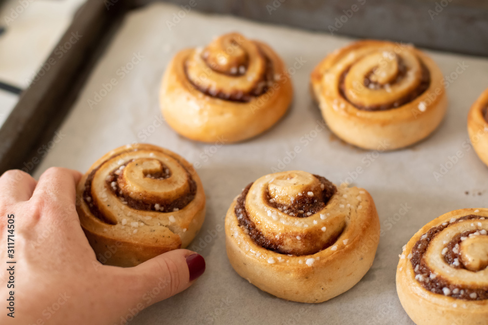 Hand taking freshly baked cinnamon buns rolls from a tray lined with baking parchment paper Hand taking freshly baked cinnamon buns rolls from a tray lined with baking parchment paper