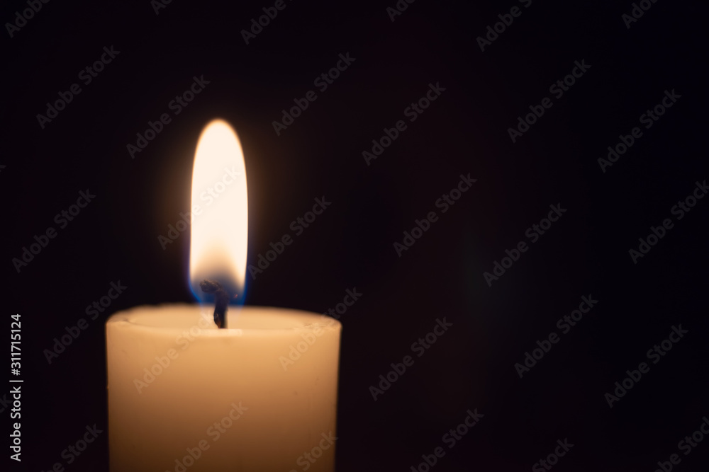 White candle with a flame on a black background close up with copy space