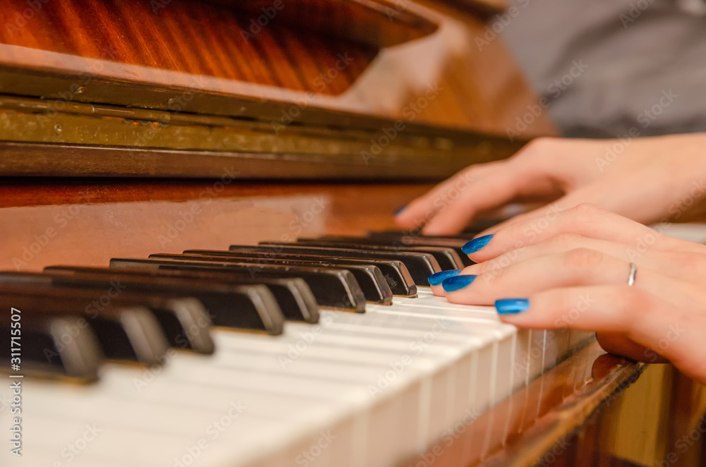 hands of a female pianist with blue nail Polish on the nails on the keys of a piano. girl playing the piano.