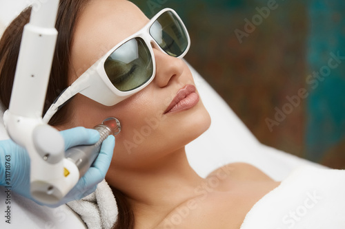 pretty woman receiving face treatment with laser wearing protection glasses