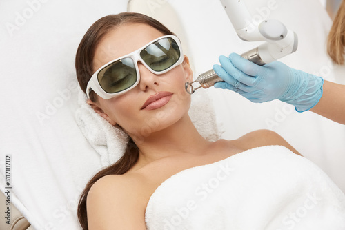 attractive woman receiving face treatment on her cheek with laser in glasses