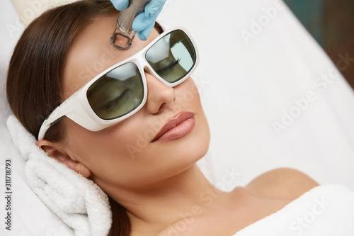 close-up of beautiful woman doing laser procedure on her forehead wearing protection glasses