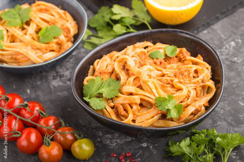Semolina pasta with tomato pesto sauce, orange and herbs on a black concrete background. Side view, selective focus