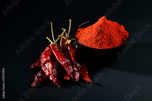 chilly powder in black bowl with red chilly, dried chillies on black background