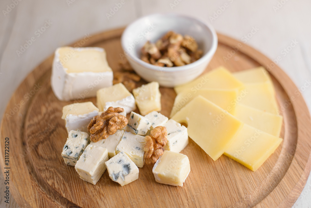 Delicious cheese plate with cheeses Dorblu, Brie, Camembert, nuts. Serving on a wooden round board. Healthy snack or aperitif for white or red wine. Selective focus, close-up