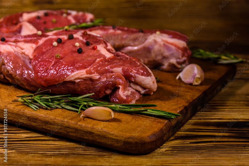 Raw ribeye steak, spices, rosemary and garlic on cutting board