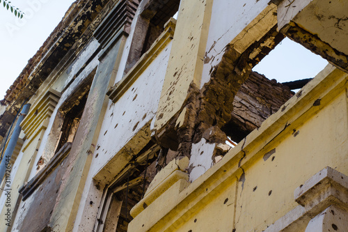 Destroyed building after hostilities. Photo of the destroyed building, the theme of the war. Military actions. Wall with holes in several places. Crumbling wall of hostilities.