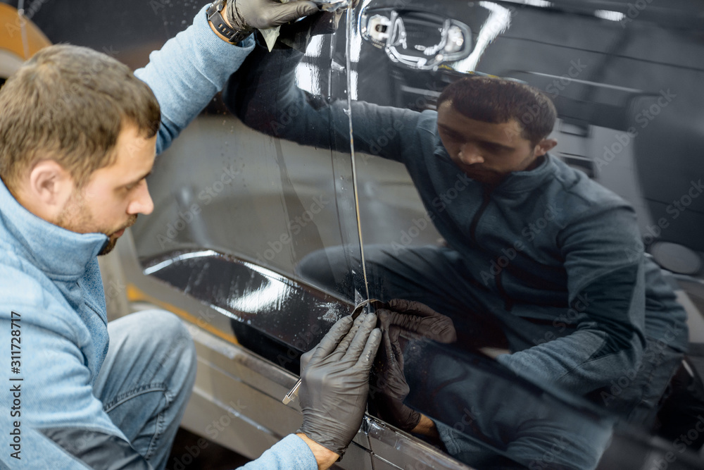Worker trimming with cutter remains of a protective film, sticking it on a car body at the vehicle service Worker trimming with cutter remains of a protective film, sticking it on a car body at the vehicle service