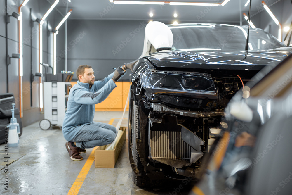 Man preparing protective film for sticking on a car body, marking it to with a pen at the vehicle service station. Concept of car body protection with special films Man preparing protective film for sticking on a car body, marking it to with a pen at the vehicle service station. Concept of car body protection with special films