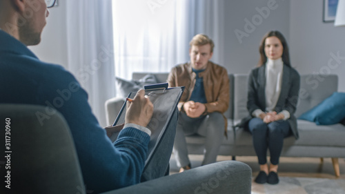 Couple on a Counseling Session with Psychotherapist. Foreground Focus on Back of the Therapist Taking Notes and Talking: People Sitting on the Analyst Couch, Discussing Psychological Problems