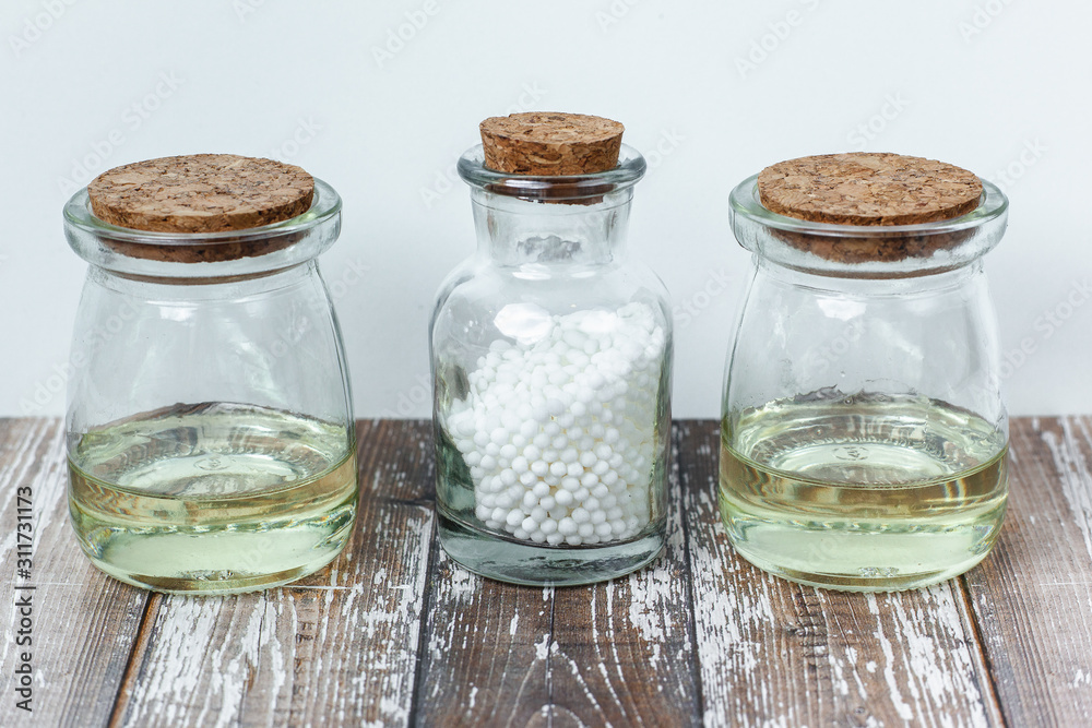 Classical Homeopathy globules lie on the leaves and vintage glass bottles on white background. Alternative Homeopathy medicine herbs, healtcare and pills concept. Place for text. Classical Homeopathy globules lie on the leaves and vintage glass bottles on white background. Alternative Homeopathy medicine herbs, healtcare and pills concept. Place for text.