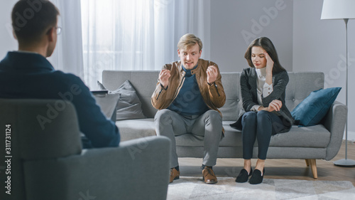 Young Couple on Counseling Session with Psychotherapist. Back View of Therapist Taking Notes: Angry Boyfriend loses Temper, Starts to Shout at His Suffering Girlfriend. Domestic Violence © Gorodenkoff