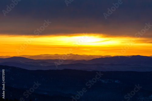 Golden sunrise in a mountain valley with beautiful contours of dark blue outlines of the highlands. landscape with a mountain landscape horizon in the style of the artist " Roerich"