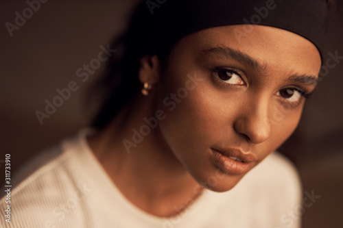 portrait of a beautiful dark-skinned girl with brown eyes looking into the camera, she has a black headband on her head and a white shirt