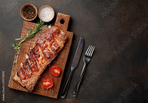 grilled pork ribs on a cutting board with spices on a stone background with copy space for your text