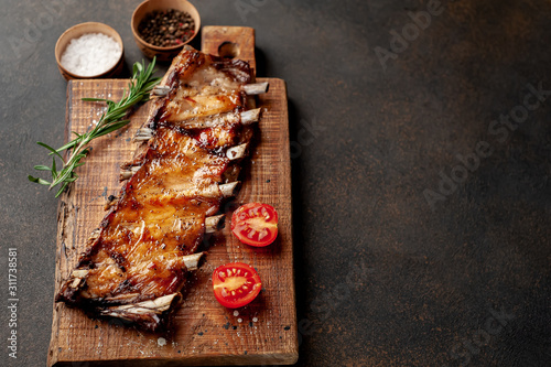 grilled pork ribs on a cutting board with spices on a stone background with copy space for your text
