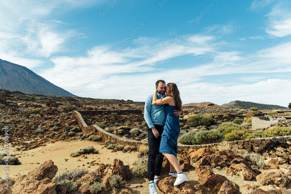 Beautiful young couple of lovers posing on a rocky field on a background of a volcano