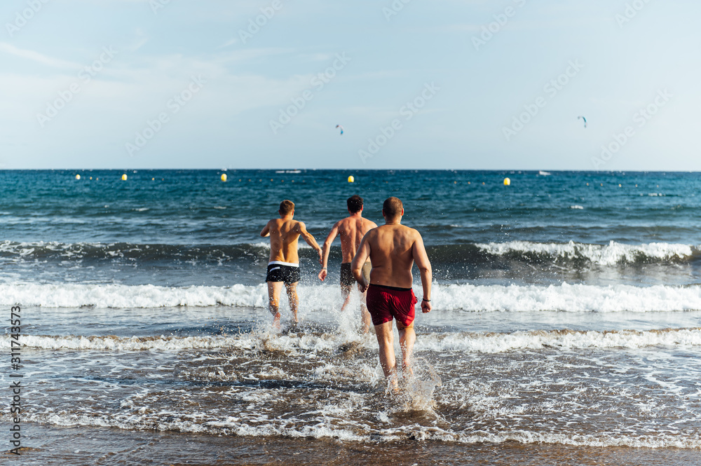 Three Caucasian friends running at sea with splash for swimming in sunset background