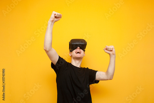 emotional guy with VR glasses wins a virtual game, a gamer rejoices victory over a yellow background