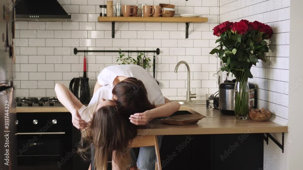 A young lesbian gently kisses her partner at home on the kitchen table