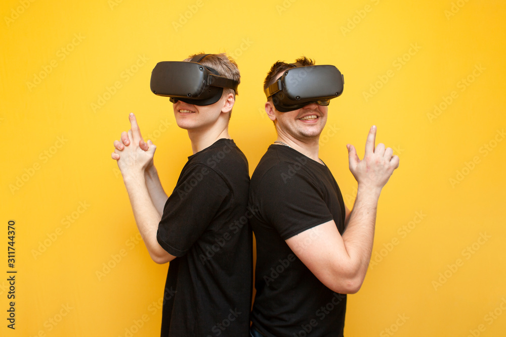 two guys in VR glasses on a yellow background, friends gamers in virtual reality glasses play a shooter and hold weapons two guys in VR glasses on a yellow background, friends gamers in virtual reality glasses play a shooter and hold weapons