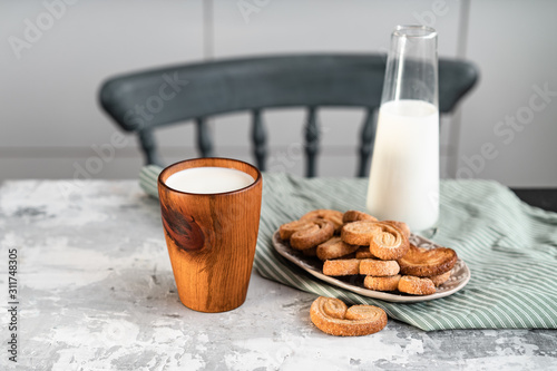 A wooden glass with milk on the kitchen table near to cookies