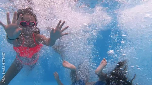 Children enjoying summer vacation. Happy fun loving group of friends jumping and diving into swimming pool at a pool party in summer sunny day. Slow motion. Underwater view photo