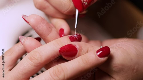 4k Caucasian hands of manicurist draws snowflake on client's red nail. Nails treatment. Nail art painting 