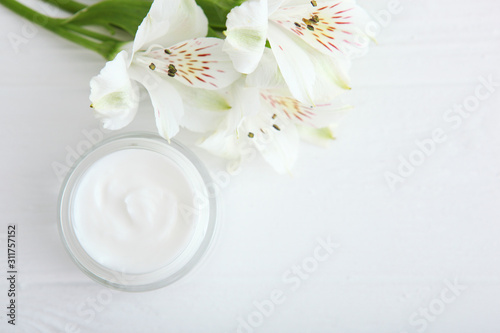 Care cream and flowers on a light background top view. Skin care cosmetics.