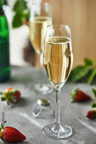 Glasses with champagne and strawberries on a gray background, with green leaves in the background