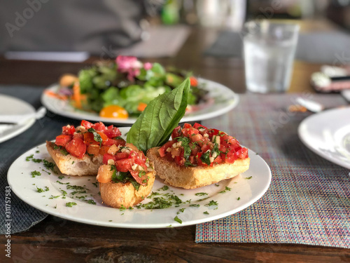 Traditional italian appetizer name Bruschetta with tomatoes, mozzarella cheese and basil on a white ceramic plate.