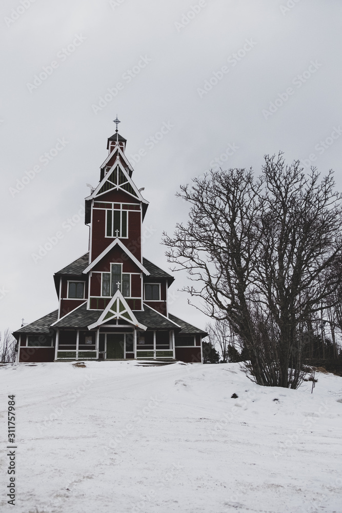 A church on a hilltop covered with snow and big tree. Beautiful wooden church Nordic style. Buksnes church, Lofoten Islands, Norway.