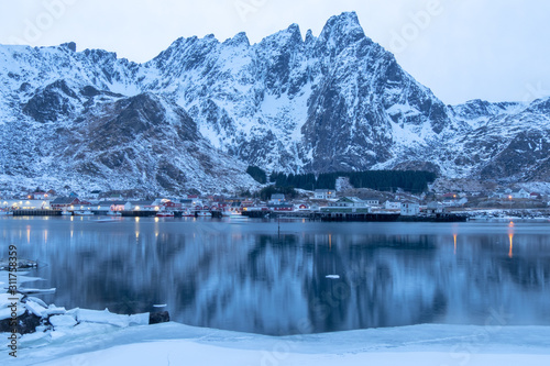 Dock in the winter season. The background is a high mountain with snow and the reflection on the water mysterious evening atmosphere. Reine, Lofoten Islands, Norway.