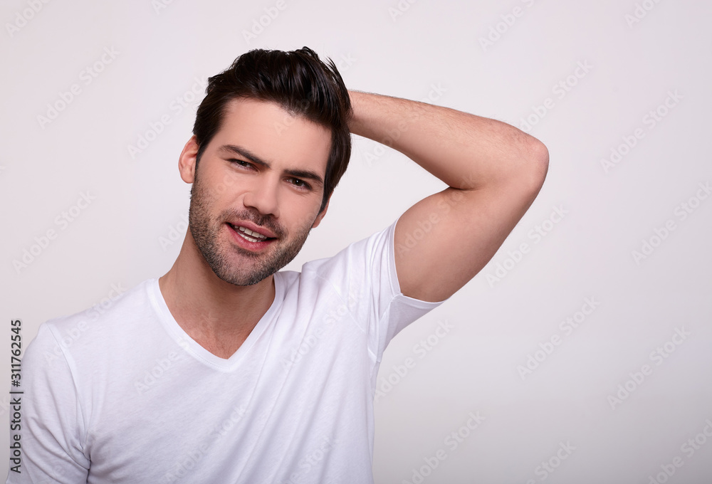 Man looking away and keeping hands behind head while standing against gray background. Man looking away and keeping hands behind head while standing against gray background.