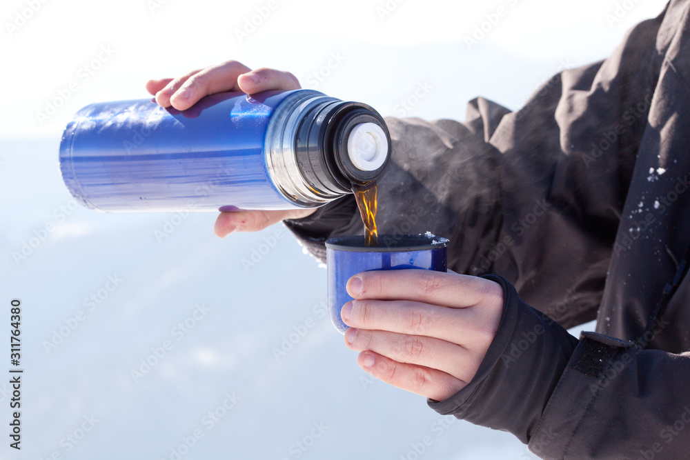 Mans hands pouring fresh hot tea from thermos to cup