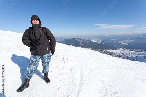 Photographer standing with camera on hill with panoramic view of winter valley