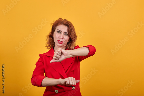 Disappointed caucasian young woman dancing, showing fists at camera wearing fashion red jacket over isolated orange background. People lifestyle concept.