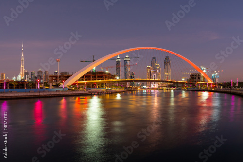 Panoramic night view on Dubai at blue hour, showing Bridge of tolerance and iconic buildings and construction cranes