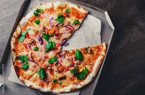 Pizza with Mozzarella cheese, onion, tuna fish, tomato sauce, pepper, basil. Italian pizza in the in delivery cardboard box on wooden table background