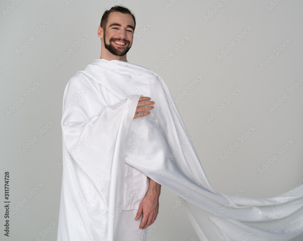 a guy joyful laughing in white epic stands on a gray background, wrapped in white cloth with flying behind as in antiquity
