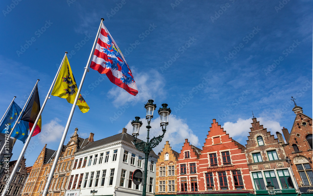 Main city square in Bruges with flags and traditional architecture. Row of colorful building in Bruges.