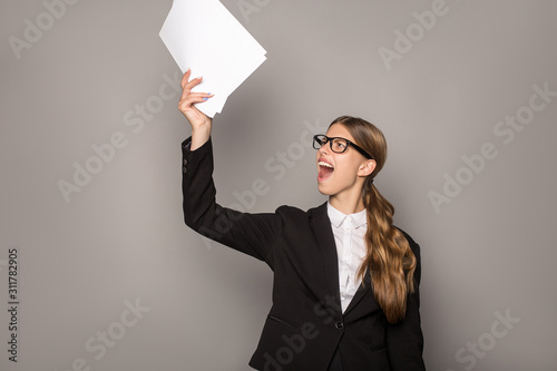 excited businesswoman holding sheets of paper isolated on grey