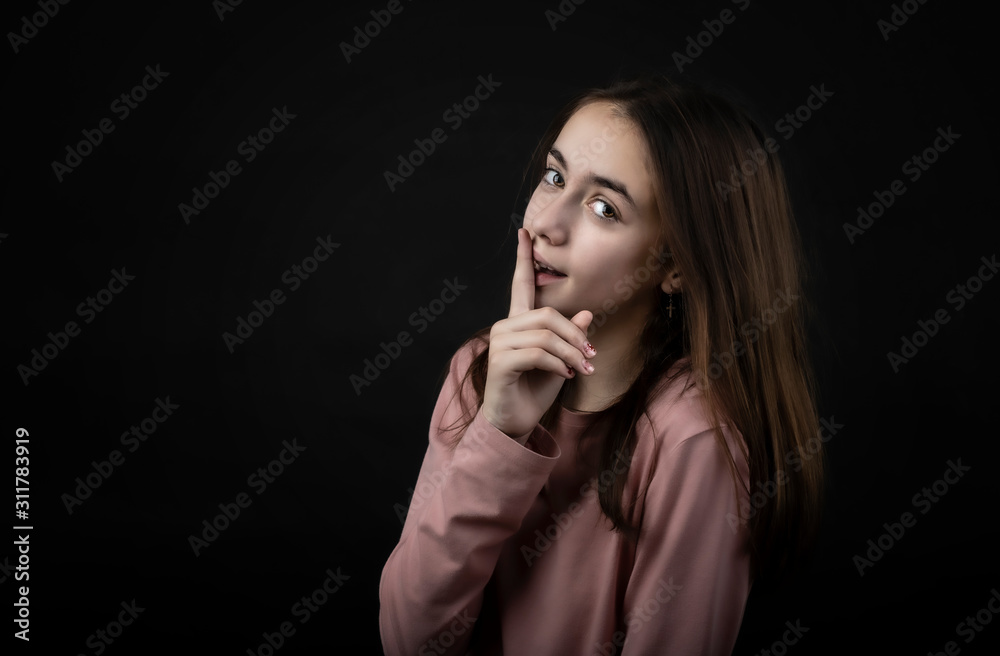 pretty girl posing in the studio with her index finger on her lips, against a dark background pretty girl posing in the studio with her index finger on her lips, against a dark background