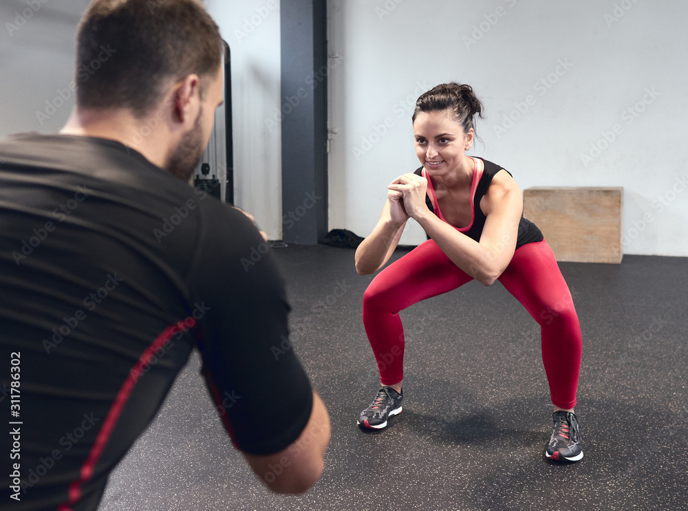 smiling young woman warming up with her personal trainer at the gym smiling young woman warming up with her personal trainer at the gym